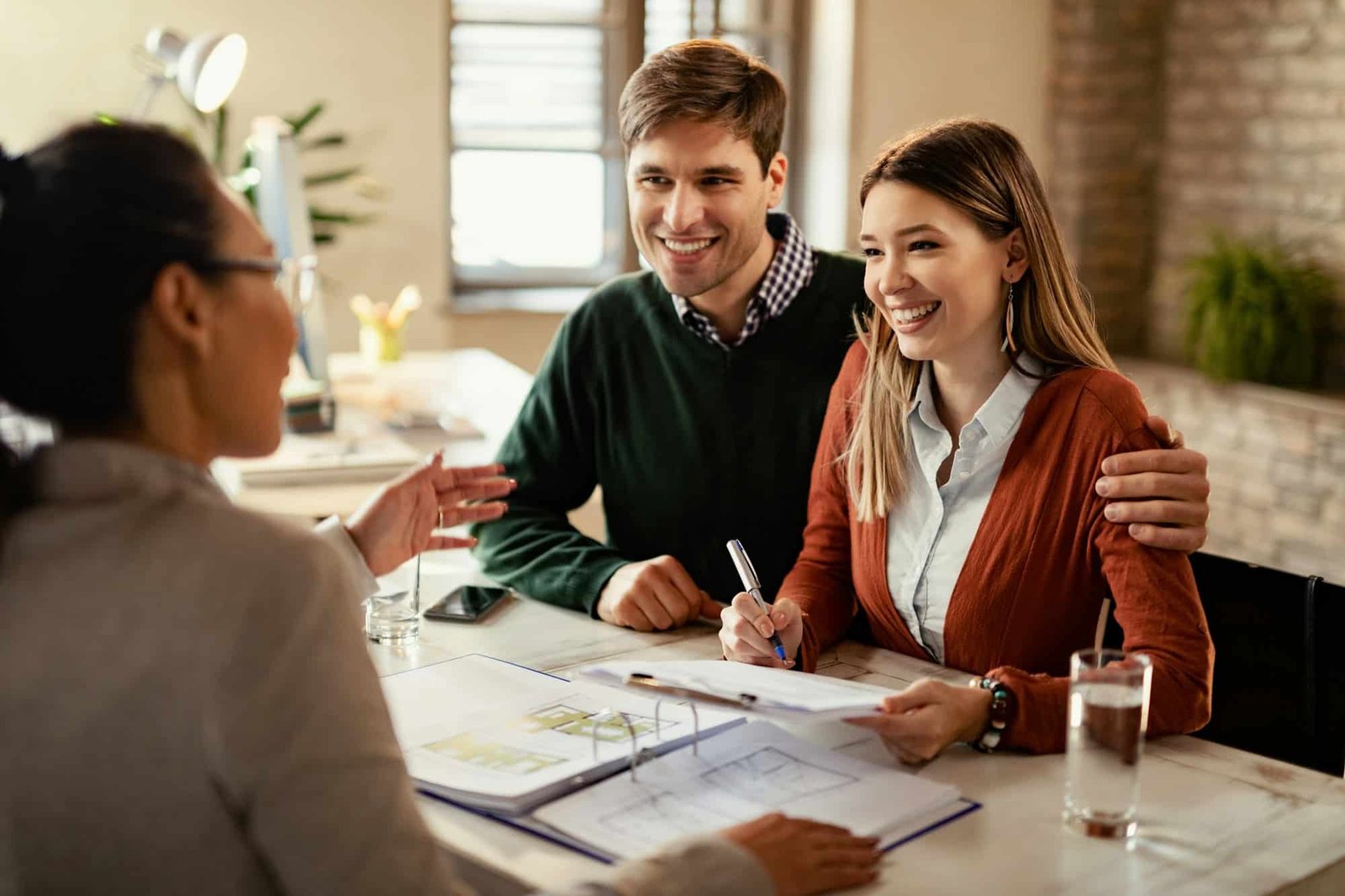 Happy couple signing mortgage contract while having meeting with real estate agent.